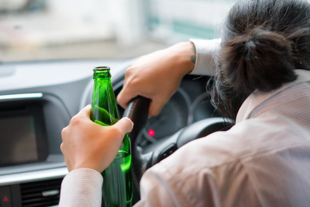 Drunk young man driving a car with a bottle of beer.