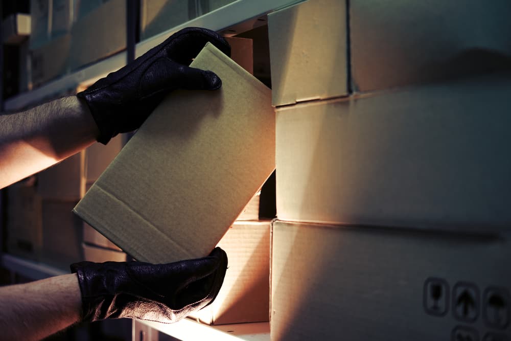 Thief hands with gloves steal a box of goods in a warehouse in the dark