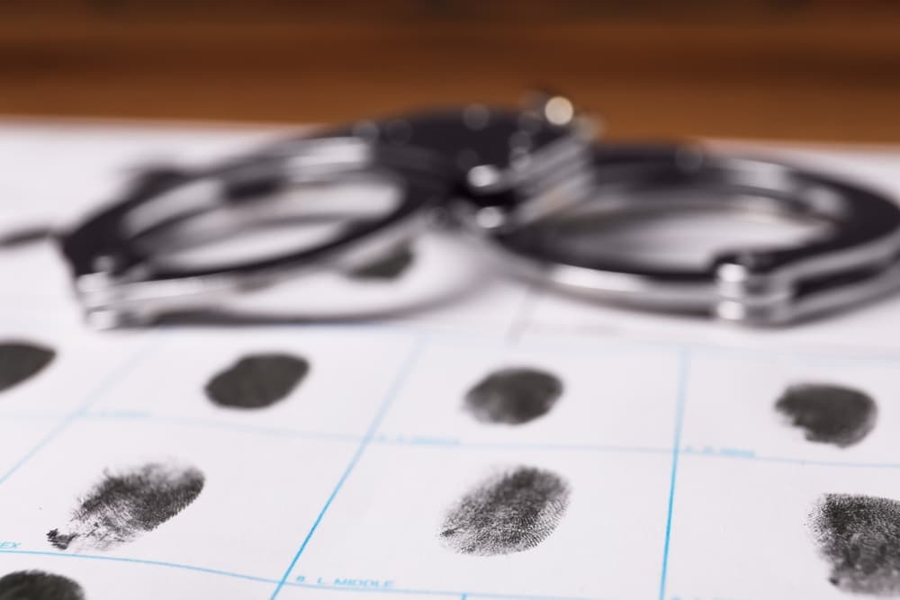 Paper sheet with human fingerprints and handcuffs on table