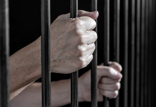 Hands gripping the bars of a jail cell in a close-up view, symbolizing imprisonment.