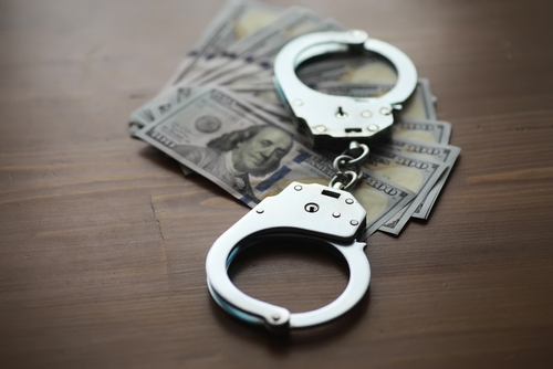 A pair of handcuffs resting on a stack of hundred-dollar bills on a wooden table.